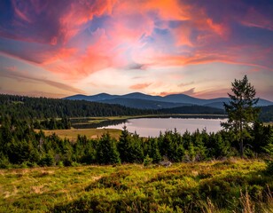 Obraz premium Vibrant sunset over a tranquil lake surrounded by lush greenery and mountains
