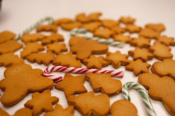 Rows of freshly baked gingerbread cookies shaped like trees and stars lay intertwined with candy canes. These festive treats are prepared for a joyful Christmas celebration in a warm kitchen.