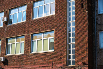 Fototapeta premium Lower part of an old red brick industrial building with damaged masonry, rusted metal door, and cracked plaster near the foundation. The photo emphasizes facade decay, material erosion, and neglected
