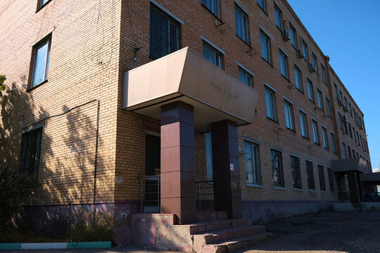 Old brick office building with numerous mounted air conditioning units and partially damaged facade plaster. The image highlights issues of exterior maintenance, insulation wear, and outdated facade