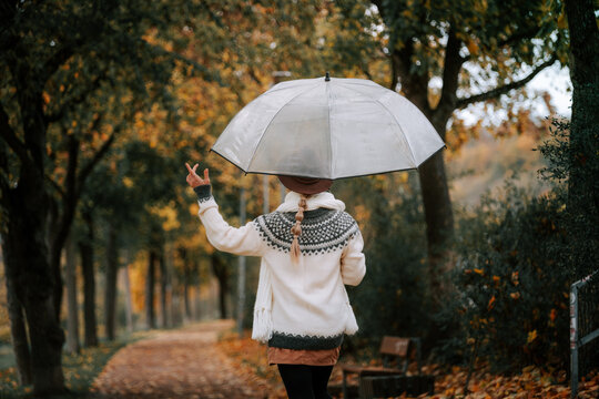Happy woman under transparent umbrella walking in autumn park smiling surrounded by falling golden leaves