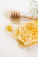 Fresh Honey in honeycombs dripping, pouring from a wooden honey dipper spoon, on white background. Honeycomb close-up. Healthy organic liquid honey spill, with tiny flowers, vertical image 