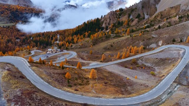 Drone view of French Alps in autumn, Col d Izoard mountain pass in autumn with golden larch trees and a winding road