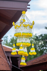 A beautiful Thai-style flower chandelier made from white and yellow flowers hanging from a wooden roof. Traditional Lanna decoration used in ceremonies and temple festivals in Thailand.