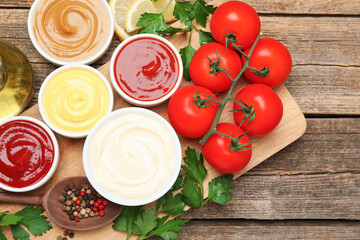 Different sauces in bowls and ingredients on wooden table, flat lay
