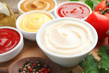 Different sauces in bowls and ingredients on wooden table, closeup