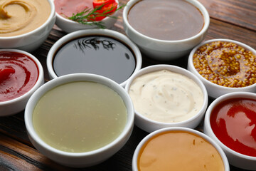 Different sauces in bowls on wooden table, closeup