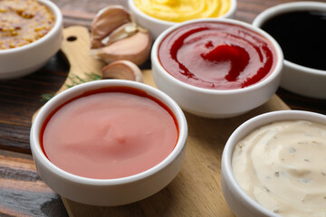 Different sauces in bowls and ingredients on wooden table, closeup
