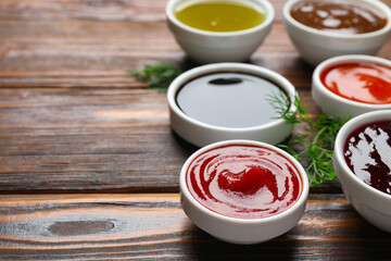 Different sauces in bowls with fresh dill on wooden table, closeup. Space for text