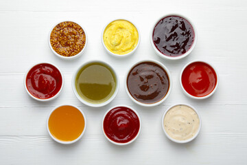 Different sauces in bowls on white wooden table, flat lay