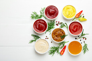 Different sauces in bowls and ingredients on white wooden table, flat lay. Space for text