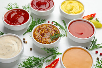 Different sauces in bowls and ingredients on white wooden table, closeup