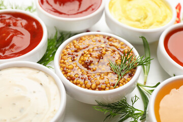 Different sauces in bowls and herbs on white table, closeup
