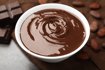 Bowl with melted chocolate, beans and pieces on grey table, closeup