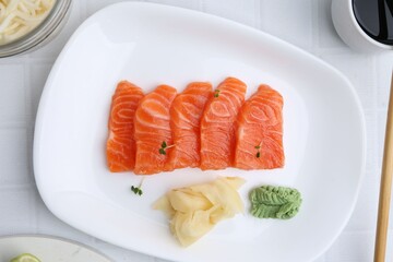 Fresh salmon sashimi with microgreens, wasabi and ginger on light tiled table, flat lay