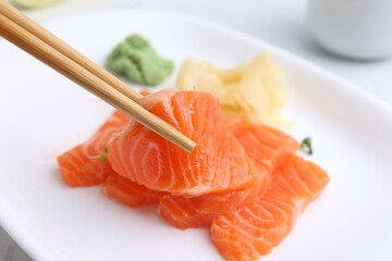 Taking fresh salmon sashimi with chopsticks from plate at light table, closeup