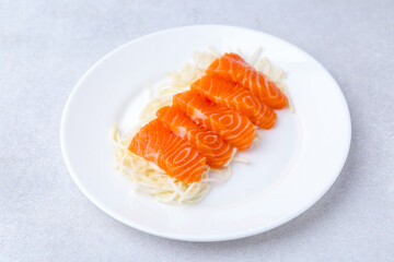 Fresh salmon sashimi with sliced radish on light grey table, closeup
