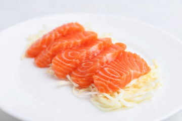 Fresh salmon sashimi with sliced radish on light table, closeup