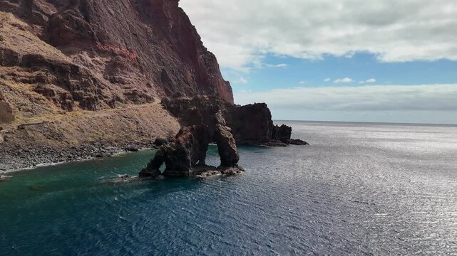 Drone view circling the majestic Roque de La Bonanza, a famous volcanic rock stack landmark off the dramatic coast of El Hierro, Canary Islands.
