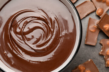 Melted chocolate in bowl and pieces with nuts on grey table, flat lay