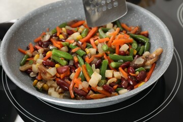 Stirring mix of fresh vegetables with slotted spatula in frying pan, closeup
