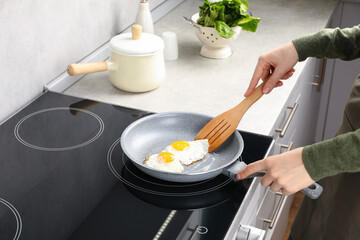 Woman taking fried eggs with slotted spatula in kitchen, closeup