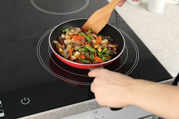 Woman stirring mix of fresh vegetables with wooden spatula in frying pan, closeup