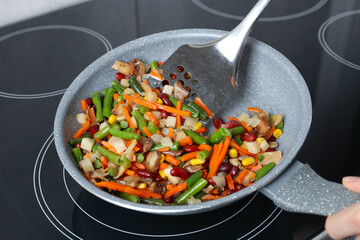Woman stirring mix of fresh vegetables with slotted spatula in frying pan, closeup
