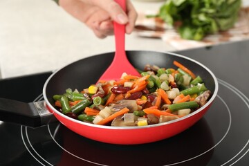 Woman stirring mix of fresh vegetables with slotted spatula in frying pan, closeup