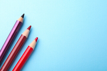 Eye pencils on light blue background, flat lay. Space for text