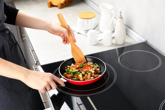 Woman stirring mix of fresh vegetables with wooden spatula in frying pan, closeup