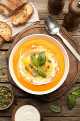 Delicious pumpkin cream soup with basil and seeds served on wooden table, flat lay