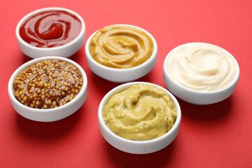 Different sauces in bowls on red background, closeup