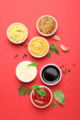 Different sauces, spices and herbs on red background, flat lay