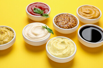 Different sauces and herbs on yellow background, closeup