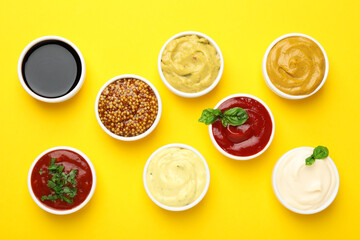 Different sauces and herbs on yellow background, flat lay