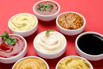 Different sauces and herbs on red background, closeup
