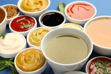 Different sauces and herbs on blue background, closeup