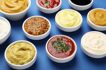 Different sauces and herbs on blue background, closeup