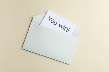 Paper note with phrase You Win! in envelope on beige background, top view