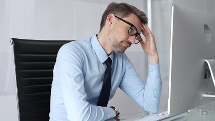 Businessman experiencing stress and headache while working on computer, feeling overworked, tired, and suffering from digital eye strain in an office setting