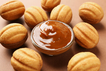 Delicious nut shaped cookies with boiled condensed milk on brown background, closeup