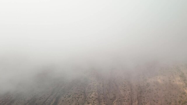 Aerial drone descent dropping sharply through a layer of swirling clouds to reveal the volcanic ravines of La Restinga and the Mar de Las Calmas coast on El Hierro, Spain.
