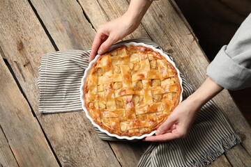 Woman with baking dish of delicious homemade apple pie at wooden table, top view