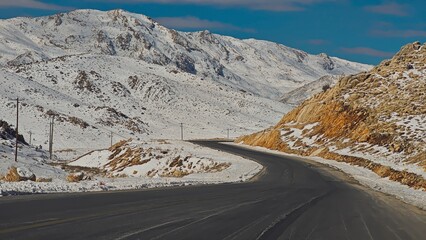 A winding road carves through a vast, rugged mountain pass blanketed with early winter snow