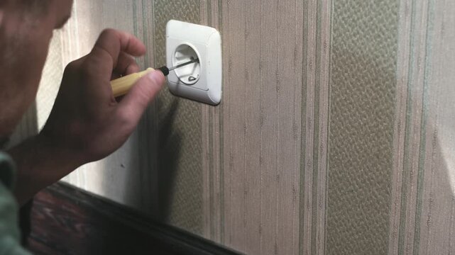 Man repairs an electrical outlet. Male unscrews an electrical outlet with a screwdriver.