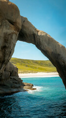 Natural rock arch above blue sea with sunlight on green cliff edge