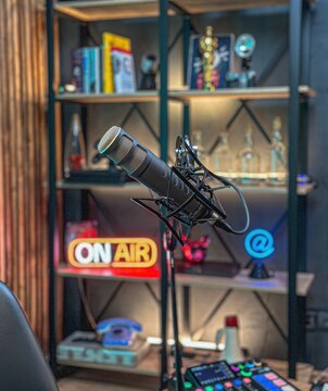A modern recording studio features a microphone in focus, illuminated ON AIR sign, and colorful shelves filled with awards and tech gadgets. Ideal for live shows or podcasts.