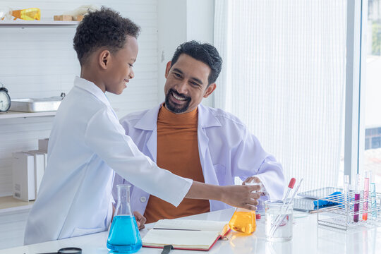 Cheerful African boy primary school students wearing lab coats studying with Indian teacher attention to chemical substance in test tube in laboratory room, lifestyle learning education science class