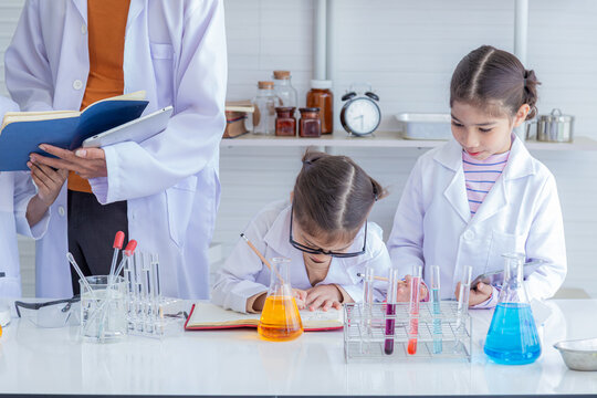 Group of multicultural African boy and elementary students girl kids friend wearing lab coat uniforms using microscope with teacher in laboratory room, lifestyle learning education in science class